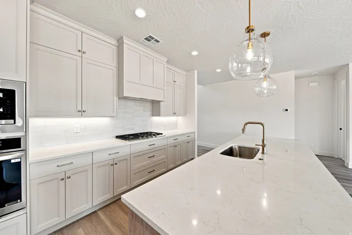 Kitchen featuring an expansive island with an undermount sink, pendant lighting, built-in stainless steel appliances, a gas cooktop, and light-toned cabinetry