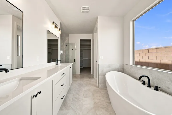 Dual vanity with integrated sinks, white cabinetry, freestanding soaking tub with matte black fixtures, and a glass-enclosed shower