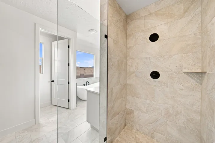 Glass-enclosed shower with tiled walls and floor, featuring matte black fixtures and an integrated corner shelf