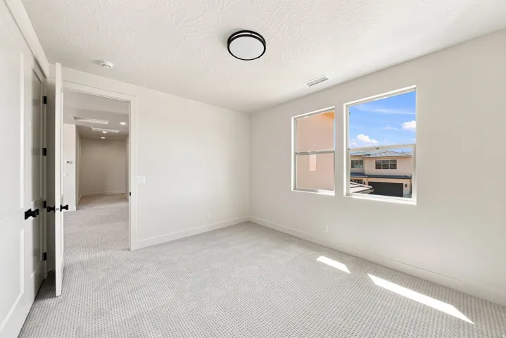Neutral tone wall paint, light-toned carpet, two windows, two panel doors with black hardware, and a ceiling-mounted light fixture
