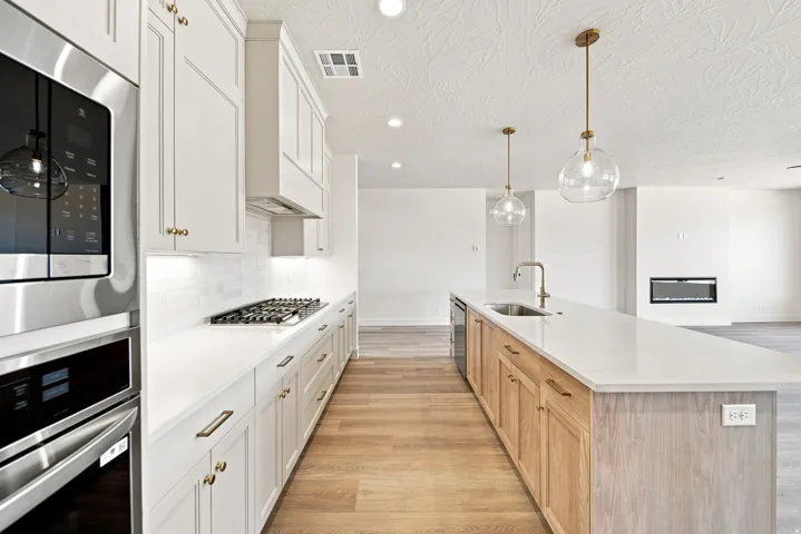 Kitchen featuring stainless steel appliances, a gas cooktop, white shaker cabinetry, an expansive island with a stainless steel sink, and wood-finish flooring