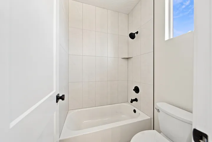White tiled shower surround with a built-in niche, matte black shower fixtures, and a white bathtub