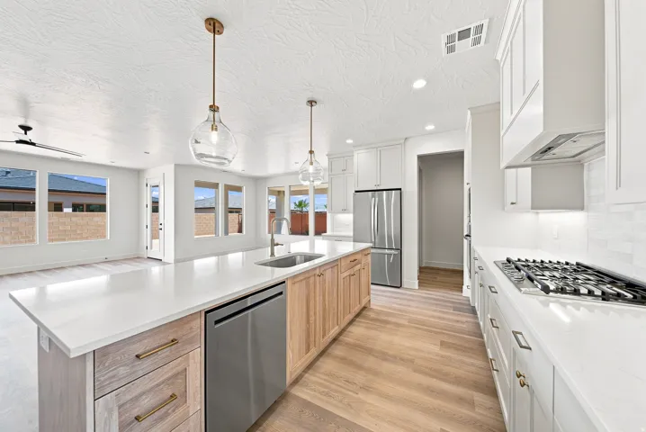 Kitchen featuring a gas range, stainless steel appliances, large center island with integrated sink, wood-finish flooring, and pendant lighting
