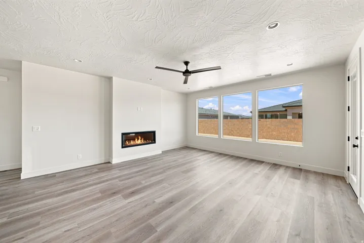 Spacious room with wood-finish flooring, a modern linear fireplace, three large windows, a ceiling fan, and recessed lighting