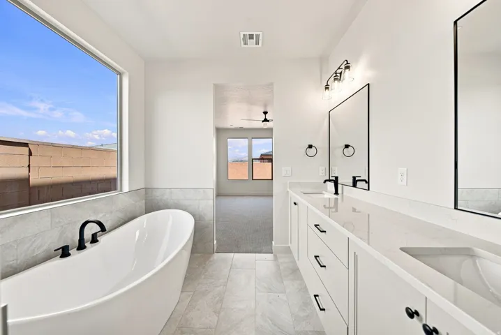 Freestanding soaking tub with matte black fixtures, dual vanity with undermount sinks and quartz countertops, tile flooring, and a large window