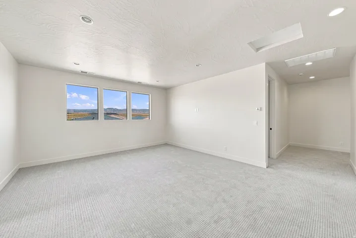 Recessed lighting, three distinct windows, light-toned carpet flooring, and a skylight