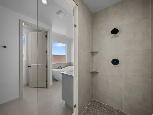 Glass-enclosed shower with large format wall tiles, hexagonal floor tiles, and matte black fixtures