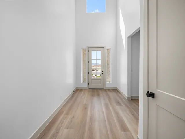 Entryway featuring a vaulted ceiling with an overhead window, wood-finish flooring, and a glass-paned door with sidelights