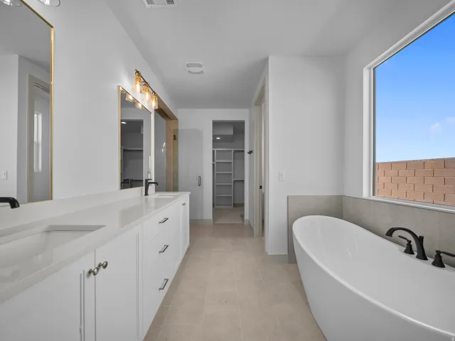 Dual vanity with white cabinetry, matte black fixtures, and gold-framed mirrors