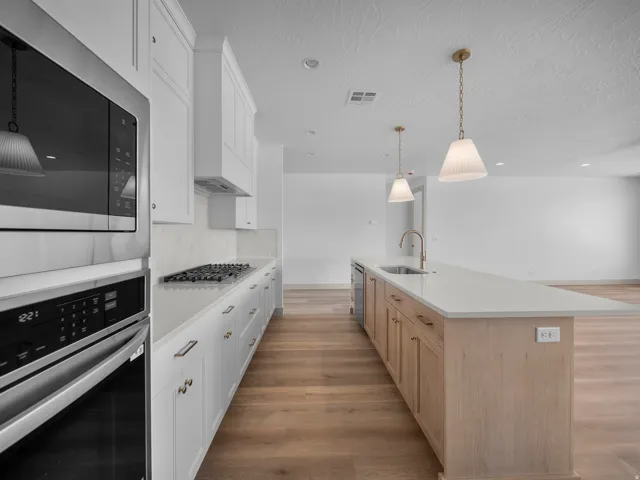 Kitchen featuring white cabinetry, integrated stainless steel appliances, wood-finish flooring, and a central island with pendant lighting