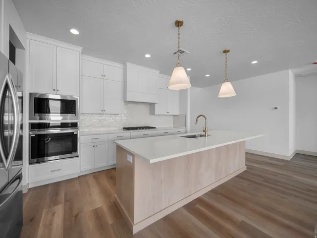 Kitchen featuring white cabinetry, stainless steel appliances, a center island with sink, pendant lighting, and wood-finish flooring