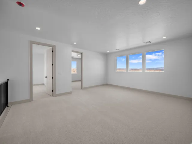 Spacious room featuring three large windows, recessed ceiling lighting, light-colored carpeting, and neutral wall tones