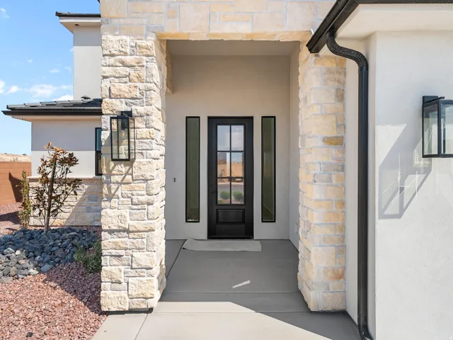 Entryway featuring stone veneer columns, a dark-framed glass panel door, flanking vertical windows, and modern wall sconces
