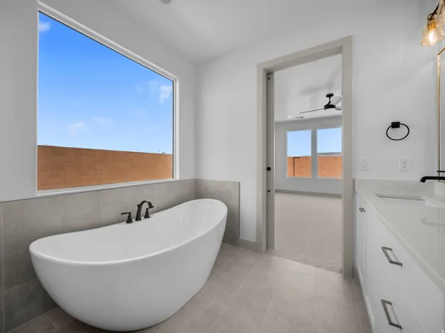Freestanding soaking tub with matte black fixtures, quartz countertop vanity with undermount sink, tiled flooring, and a large horizontal window