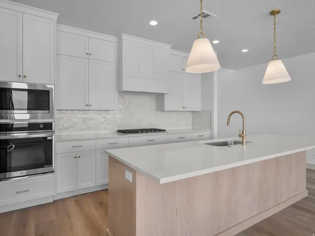 Modern kitchen featuring white cabinetry, stainless steel appliances, a tile backsplash, and a large island with an undermount sink and brass-finish faucet