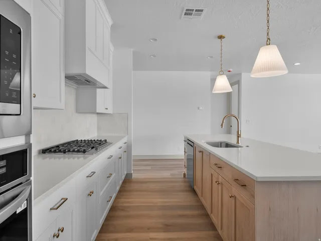 Kitchen featuring stainless steel appliances, white cabinetry, a built-in gas range, a central island with an undermount sink, and wood-finish flooring