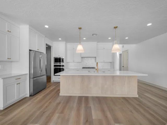Bright kitchen featuring recessed lighting, white cabinetry, a central island with a light wood-finish base, stainless steel appliances, and wood-finish flooring
