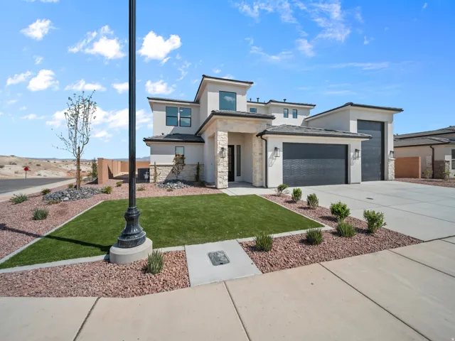 Stucco exterior with stone accents, dark garage doors, concrete driveway, artificial turf, and desert landscaping
