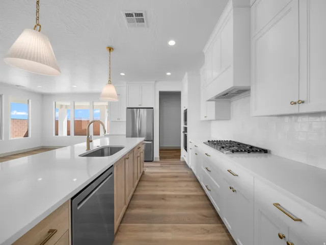 Gourmet kitchen featuring white shaker cabinetry, an expansive island with a stainless steel sink, wood-finish flooring, a gas range, and integrated stainless steel appliances