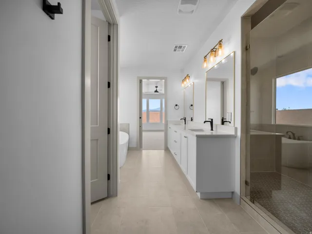 Spacious bathroom featuring dual vanities with white cabinetry, quartz countertops, matte black fixtures, a glass-enclosed shower with mosaic tile flooring, and a freestanding soaking tub