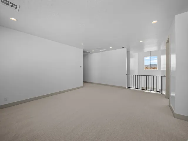 Spacious room featuring neutral carpet flooring, recessed lighting, white painted walls, and a black wrought iron railing