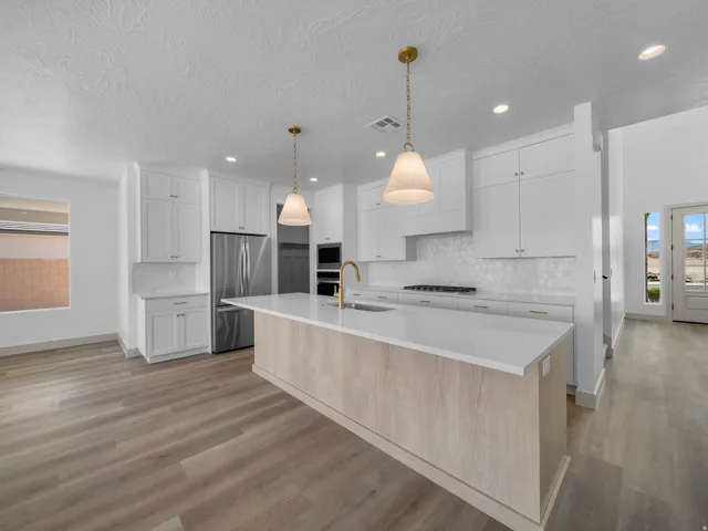 White shaker cabinetry with gold-tone hardware, stainless steel appliances, wood-finish flooring, and a central island with a light wood-finish base and white countertop