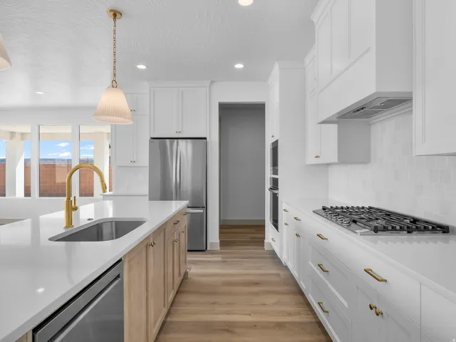 Modern kitchen featuring white cabinetry, light wood-finish flooring, stainless steel appliances, a gas cooktop, and a kitchen island with an undermount sink