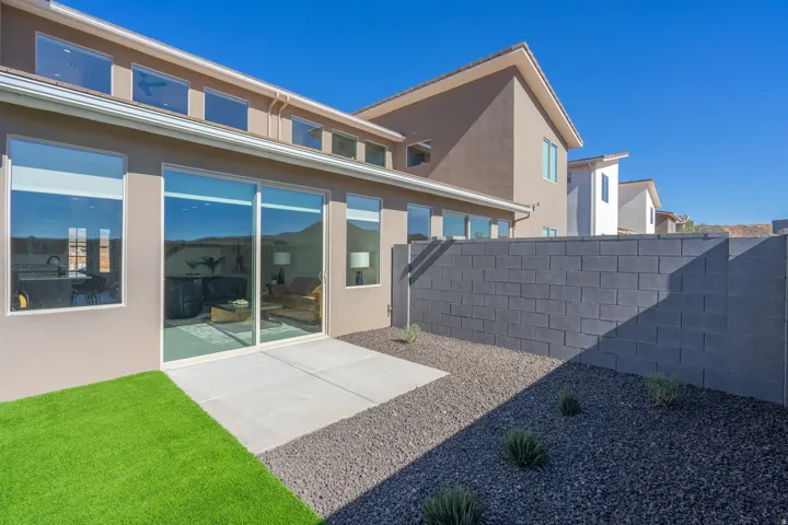 Modern home exterior showcasing a spacious rear patio with concrete decking, manicured lawn, and drought-resistant landscaping