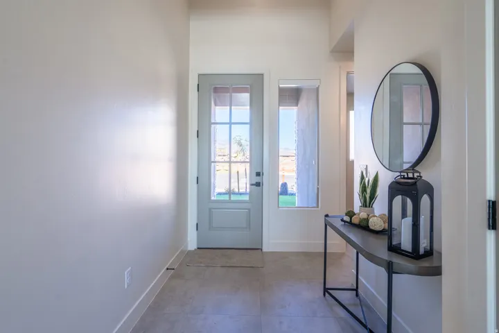 Bright entryway featuring dual glass-paneled doors with natural light, polished concrete flooring, and a modern oval mirror mounted above a sleek black console table with geometric base