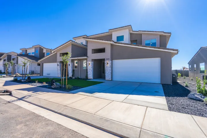 Contemporary exterior featuring a two-car garage, multi-toned stucco, and stone accents
