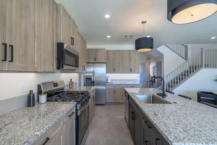 Gourmet kitchen featuring granite countertops, stainless steel appliances, wood-finish cabinetry, a subway tile backsplash, and a large center island with an undermount sink