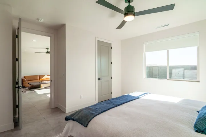 Bright secondary bedroom with expansive windows framing natural light, neutral carpet flooring, ceiling fan with integrated lighting, and direct access to an ensuite bathroom featuring a glass-enclosed shower and neutral finishes