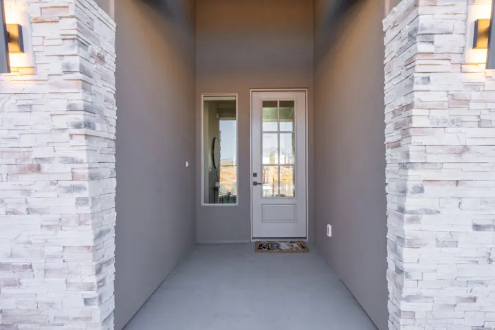 Modern entry vestibule featuring symmetrical brick pilasters with horizontal stacking detail, finished concrete flooring, and dual glass-panel doors with sidelights framed by clean architectural molding