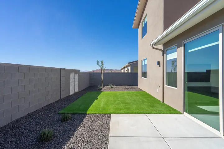 Newly landscaped backyard with lush turf lawn, decorative gravel borders, and modern concrete patio