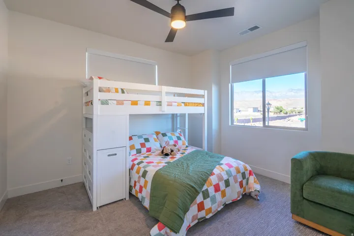 Bright bedroom featuring a white loft bed with integrated storage and desk space, carpet flooring, and dual windows with natural light