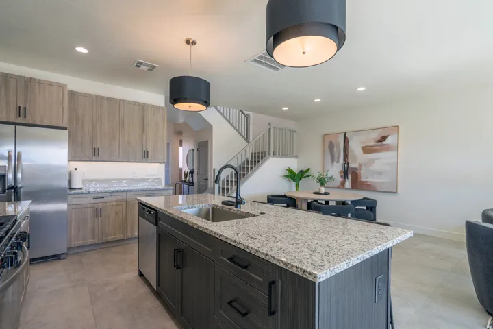 Modern kitchen featuring light wood-finish cabinetry, stainless steel appliances, and a spacious island with granite countertop and waterfall edge