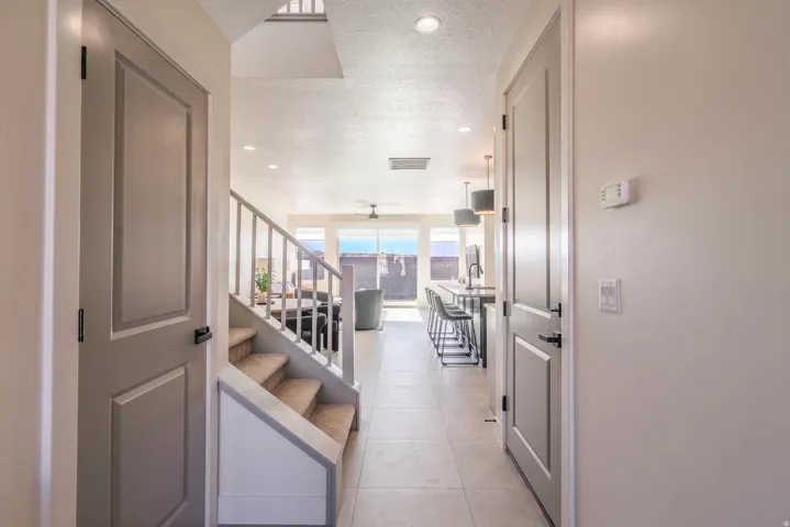 Bright hallway with recessed ceiling lighting and pendant fixtures, neutral wall finishes, and tile flooring throughout