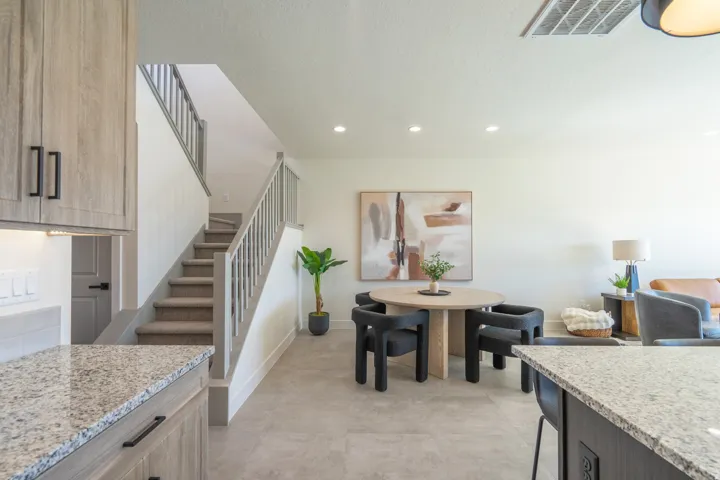 Granite countertops, wood-finish cabinetry with matte black hardware, recessed lighting, tile flooring, and carpeted stairs with a painted railing