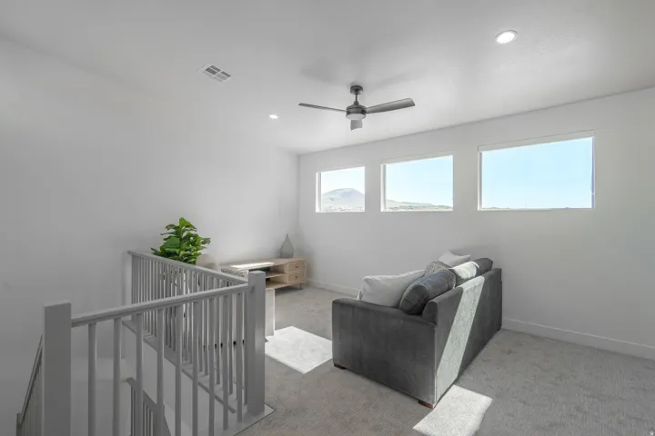 Bright, multi-window secondary bedroom featuring abundant natural light, neutral carpeting, and modern ceiling fan