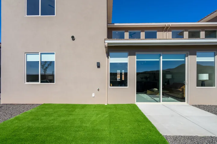Stucco exterior with multiple windows, a concrete patio, artificial turf, and dark gravel landscaping