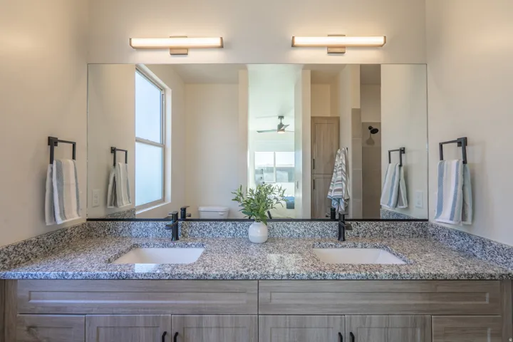 Dual-sink vanity featuring a speckled stone countertop, paired faucets with matte black fixtures, and generous storage cabinetry below