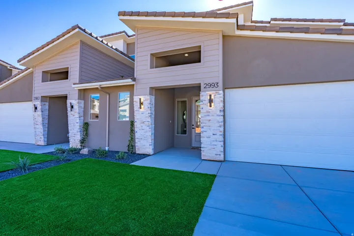Modern architectural design with stone veneer accents, integrated outdoor lighting, artificial turf landscaping, and a two-car garage