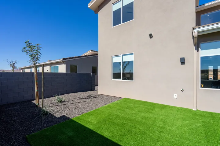 Modern home with a spacious backyard featuring manicured artificial turf, decorative rock landscaping, and a young shade tree