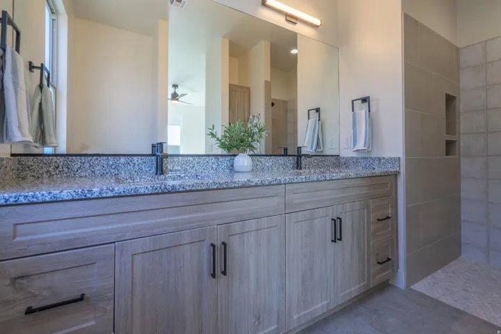 Spa-inspired primary bathroom featuring a dual-sink vanity with soft-close cabinetry in light wood finish, speckled quartz countertop, and brushed nickel hardware