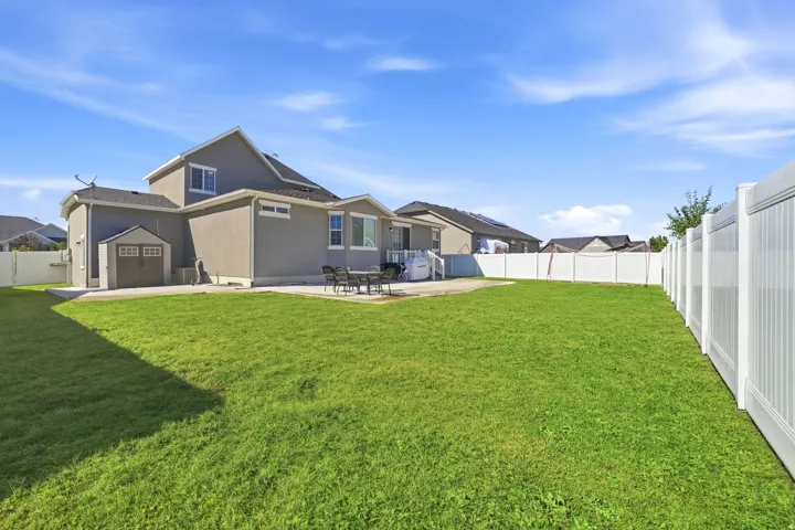 Expansive lawn, concrete patio, built-in storage shed, and full white privacy fencing