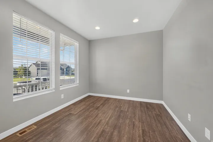 Recessed lighting illuminates the room, featuring two windows with horizontal blinds and wood-finish flooring
