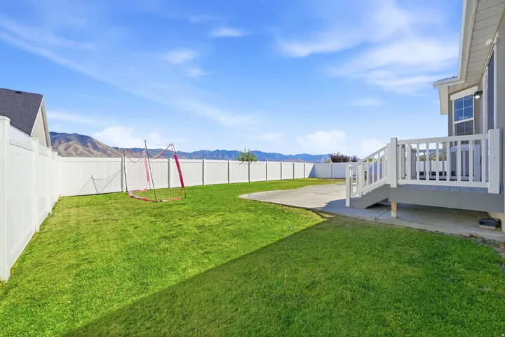 Expansive backyard featuring a manicured lawn, a concrete patio, and a white privacy fence