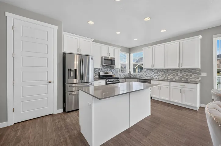 Kitchen featuring white cabinetry, stainless steel appliances, a center island with a solid surface countertop, wood-finish flooring, and recessed lighting