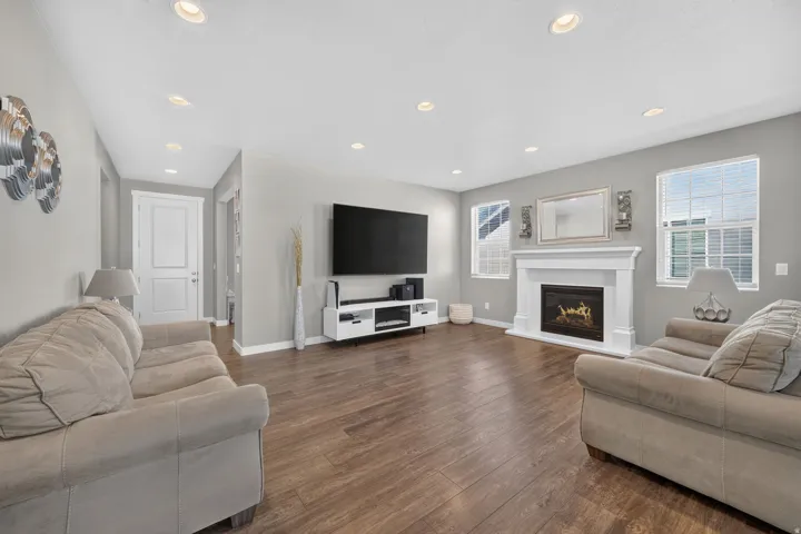 Spacious living area featuring wood-finish flooring, a decorative fireplace with a white mantel, recessed lighting, and multiple windows