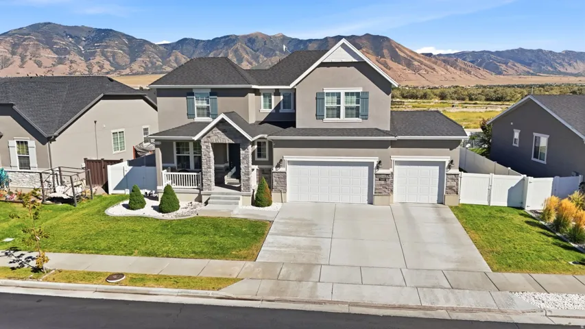 Two-story stucco exterior with stone accents, covered entry porch, dark shingle roof, two-car garage, and a concrete driveway
